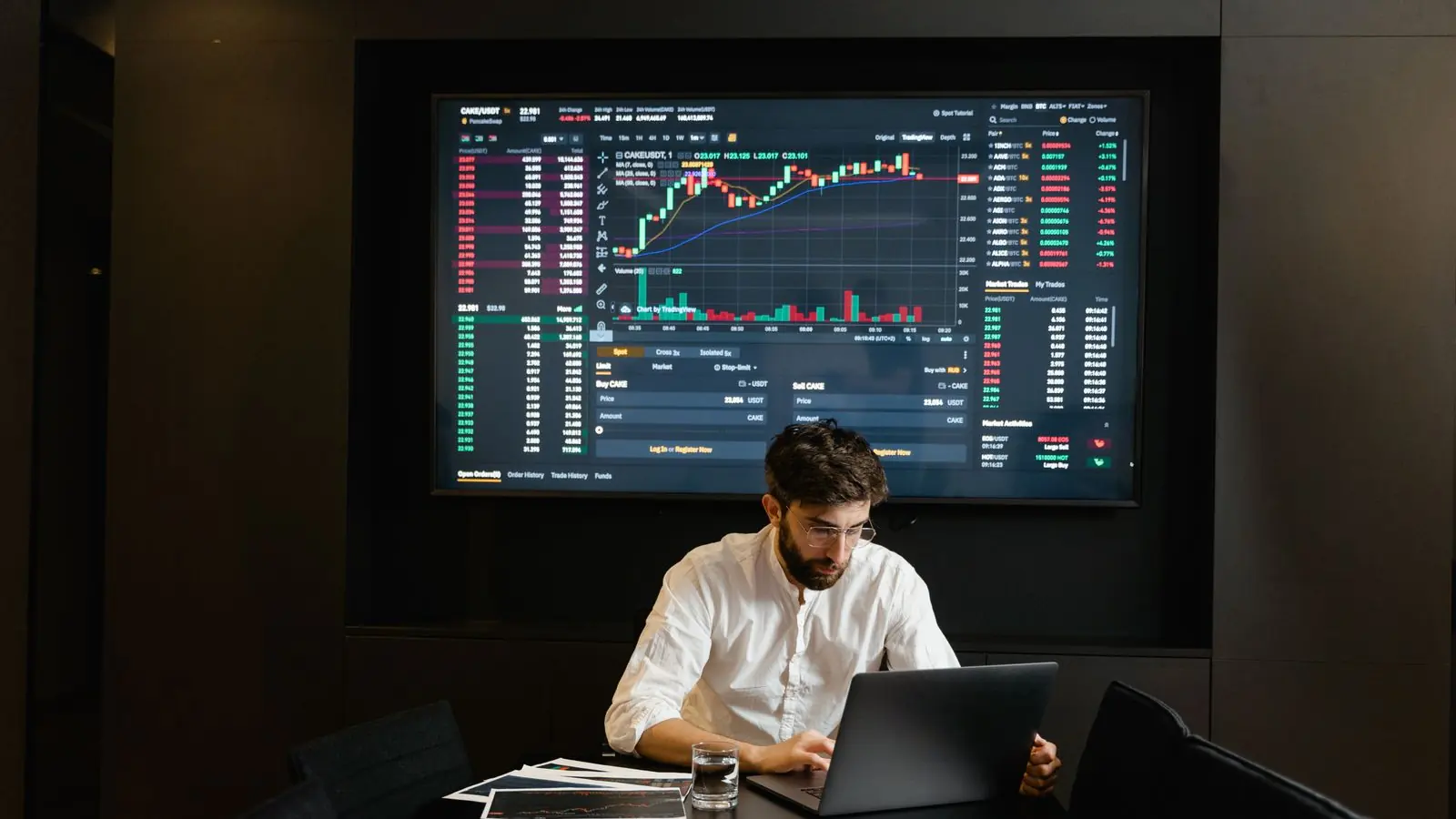 An analyst working alone at a desk in front of a wall-sized trading chart