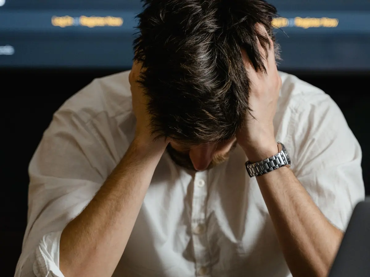 A trader sitting with their head in their hands in front of a falling chart